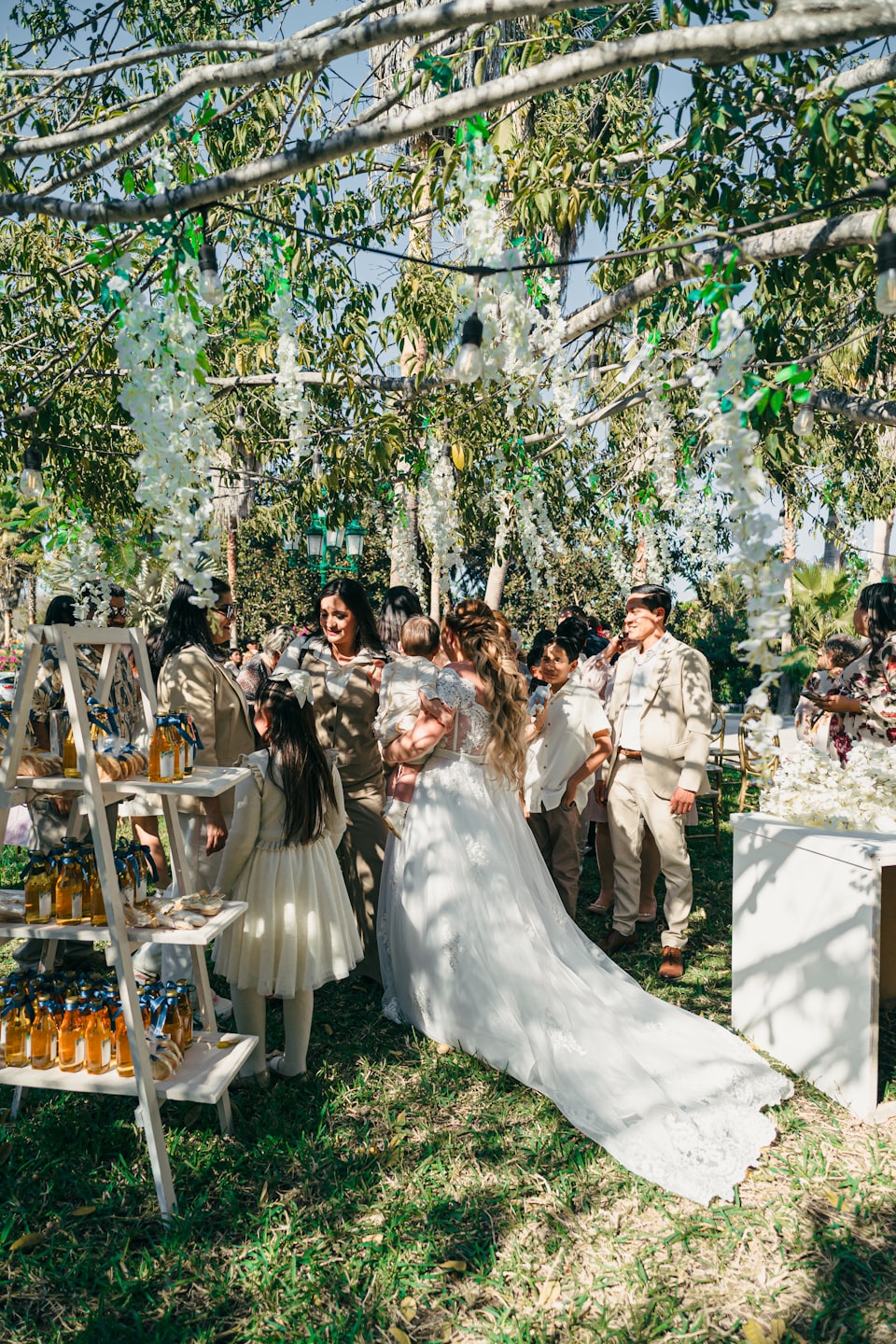 A bride holding a baby at an outdoor garden wedding reception.