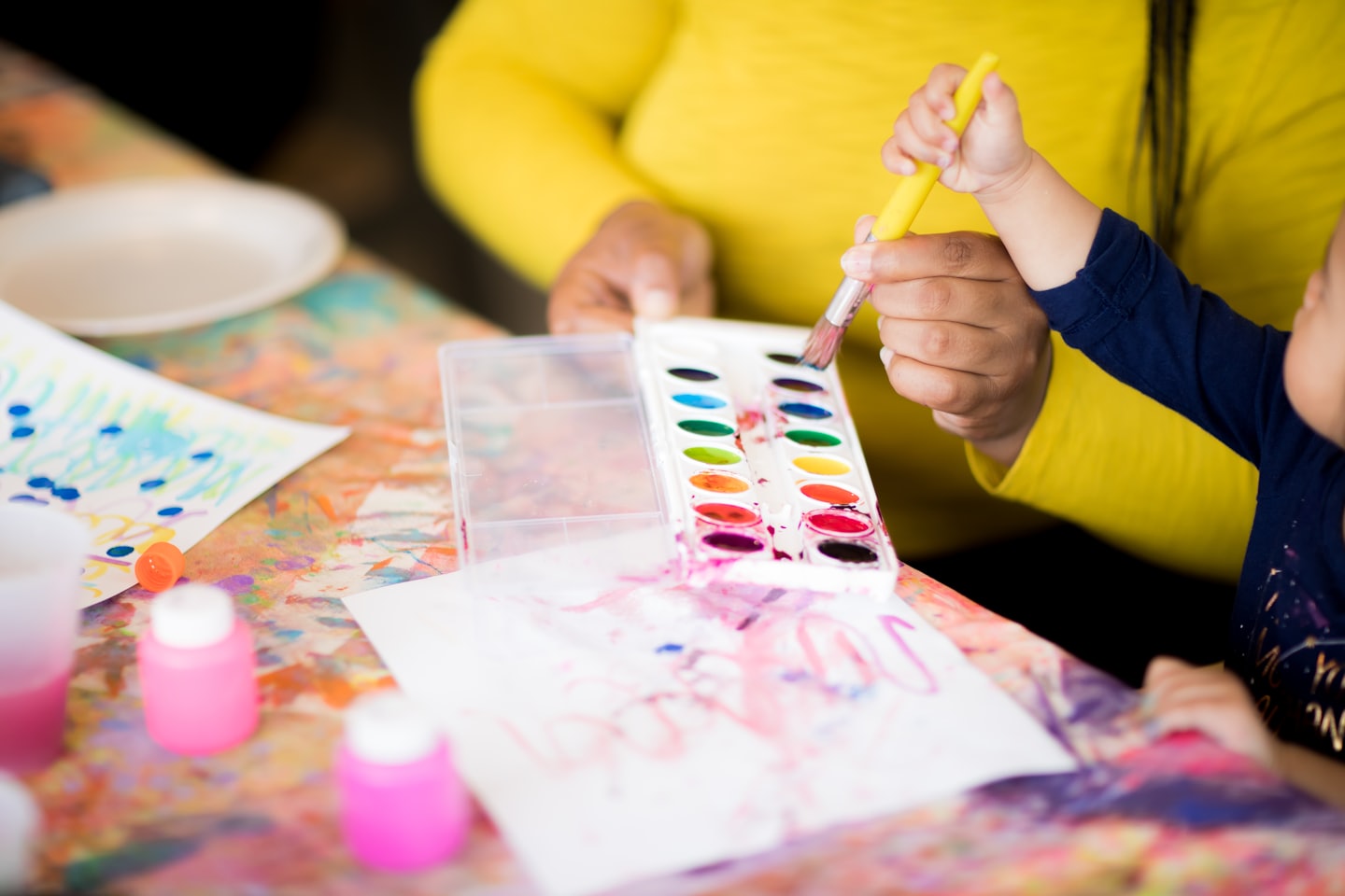 An adult guiding a child's hand while painting on paper.