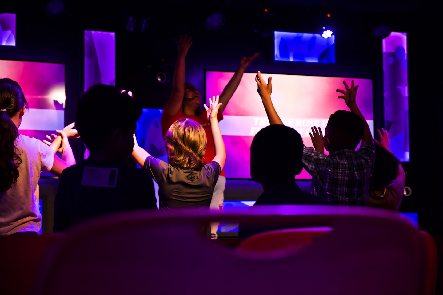 Children raise their hands during an interactive event on stage.