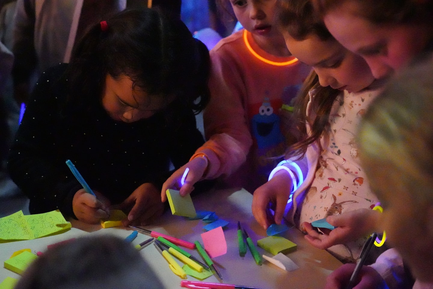 Children draw and write on colorful sticky notes at a table.