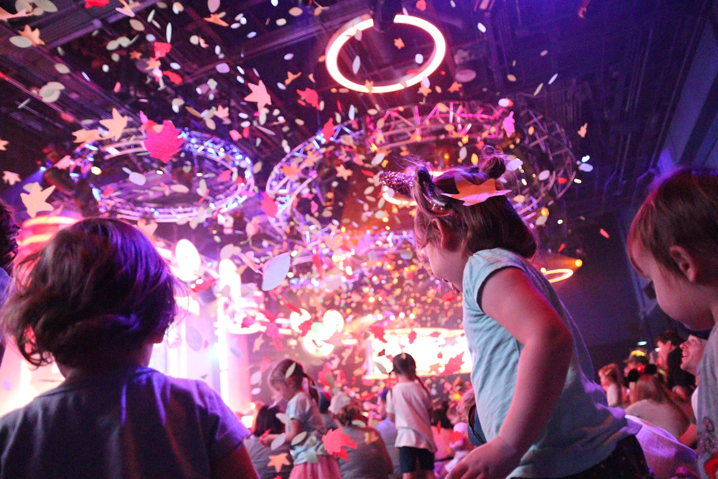 Children looking up at colorful confetti falling indoors.